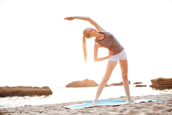 Mulher bonita esticando as mãos durante o ioga na praia — Fotografia de Stock