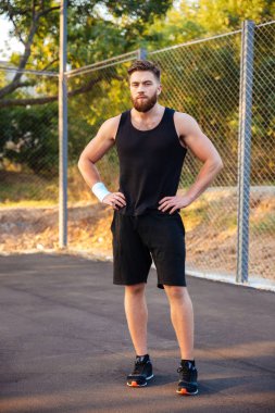 Sakallı adam spor giyim ayakta ellerle kalça üzerinde yoğunlaştı