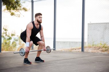 Egzersiz ve halter açık havada kaldırma adam atlet ciddi genç sakallı