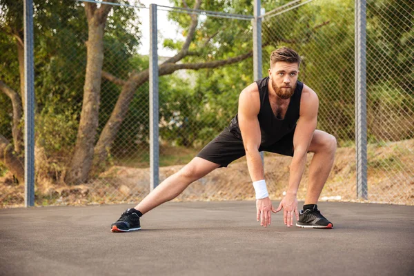 Çekici genç erkek atlet bacaklarını esnetiyor