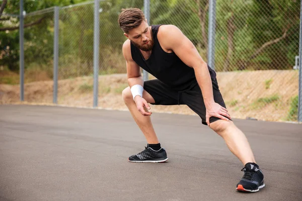 Katta oturan ve bacak germe konsantre erkek atlet