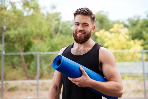 Красивый бородатый молодой спортсмен с ковриком для йоги — стоковое фото