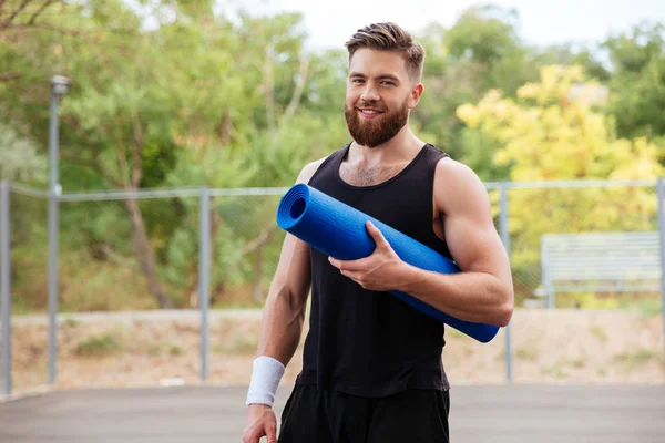 Lachende vrolijke fitness man met yoga mat permanent buitenshuis — Stockfoto