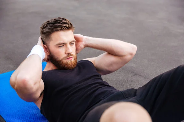 Bonito homem de esportes concentrado fazendo exercício de imprensa ao ar livre — Fotografia de Stock