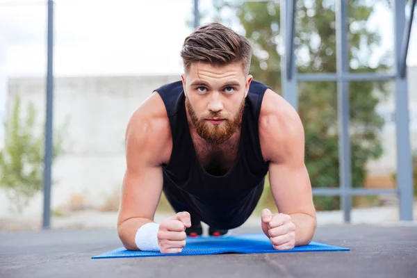 Sportsman csinál deszka gyakorlat szőnyeg kék fitness, edzés alatt — Stock Fotó