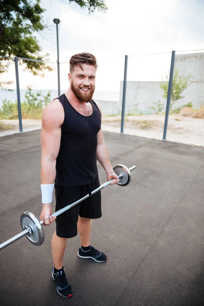 Esportista sorrindo atraente de pé e segurando barbell — Fotografia de Stock