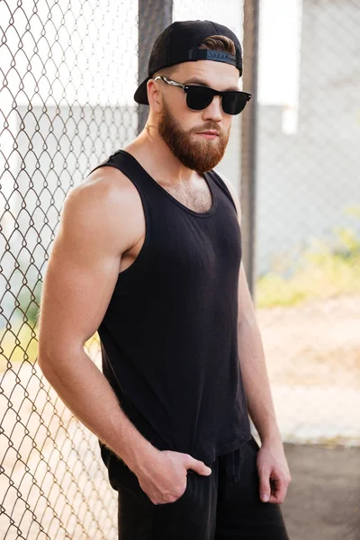 Güneş gözlüğü ve şapka giyen metal kentsel çit yaslanmış adam