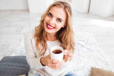 Çay bardağı tutan ve kapalı kameraya bakarak gülümseyen kız