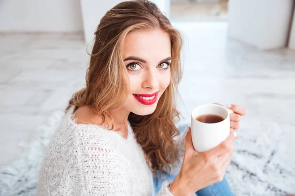 Sonriente chica atractiva en suéter sosteniendo taza de té — Foto de Stock