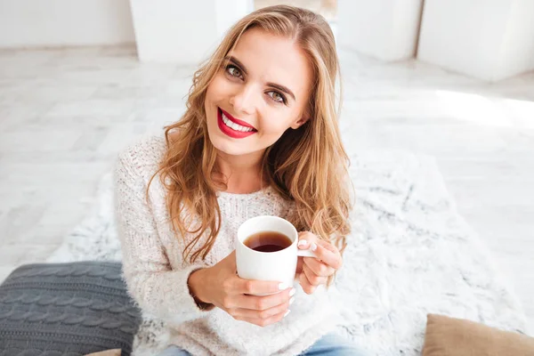 Sonriente chica sosteniendo la taza de té y mirando a la cámara en el interior —  Fotos de Stock