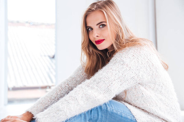 Красивая молодая женщина в свитере сидит на полу
