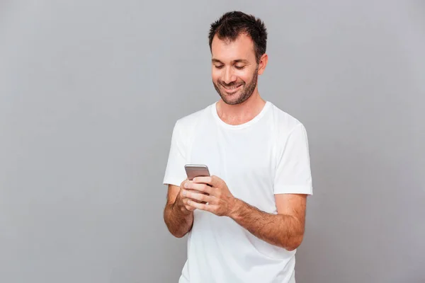 Leende ung man i vit skjorta med smartphone — Stockfoto