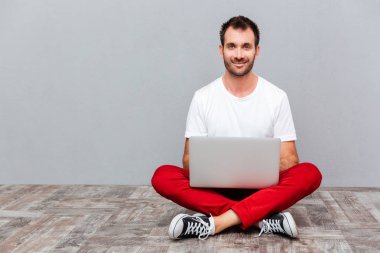 Dizüstü bilgisayar ile katta oturan mutlu casual adam