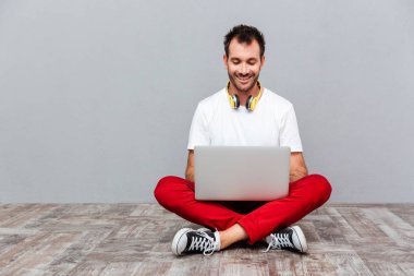 Mutlu casual adam yerde otururken dizüstü bilgisayar kullanarak