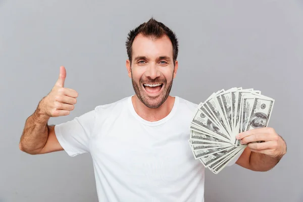 Lycklig framgångsrik ung man hålla pengar och visar tummen upp — Stockfoto