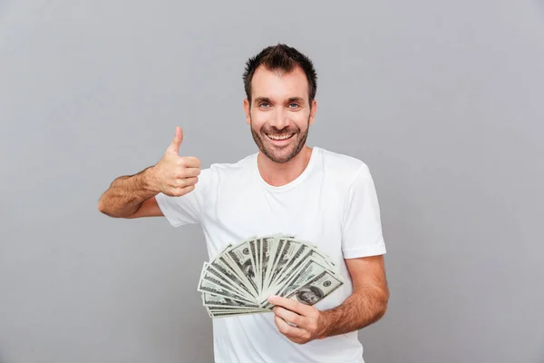Glada framgångsrik ung man hålla pengar och visar tummen upp — Stockfoto