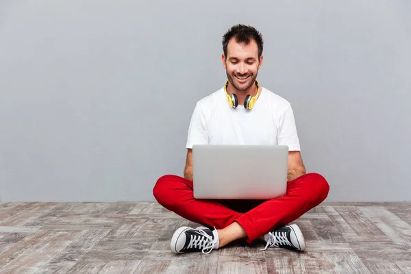 Homem casual feliz usando laptop enquanto sentado no chão — Fotografia de Stock