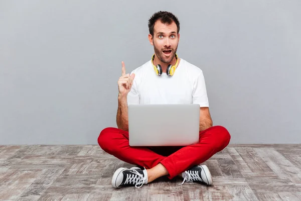 Man zittend op de vloer met laptop en vinger omhoog — Stockfoto