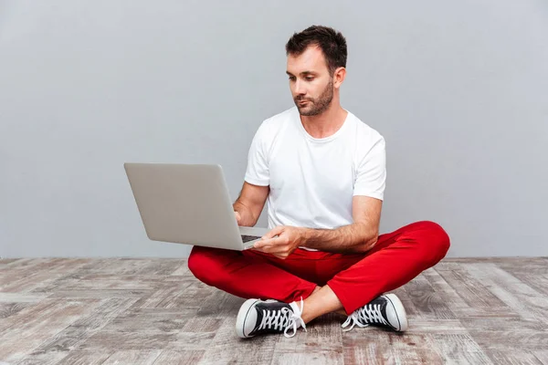 Pensivo homem casual sentado no chão com laptop — Fotografia de Stock