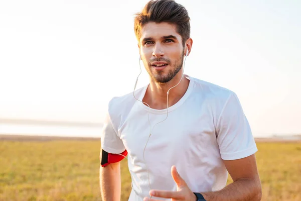 Handsome sportsman running outdoors and listening to music with earphones — Stock Photo, Image