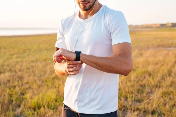 Homem de esportes olhando para seu smartwatch com fones de ouvido — Fotografia de Stock