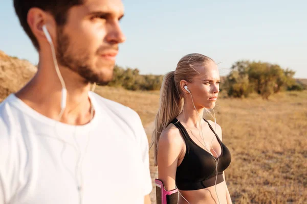 Joven pareja de fitness de pie junto con auriculares y mirando hacia otro lado — Foto de Stock