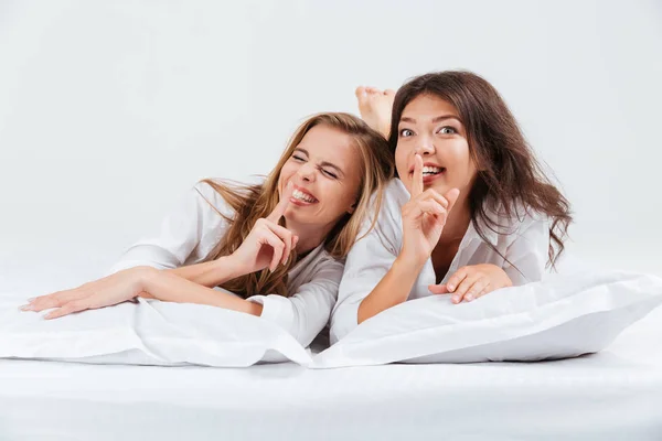 Mujeres acostadas en la cama y mostrando gesto de silencio con el dedo —  Fotos de Stock