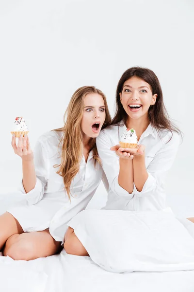 Dos mujeres sonrientes felices en camisas blancas comiendo pastelitos dulces —  Fotos de Stock