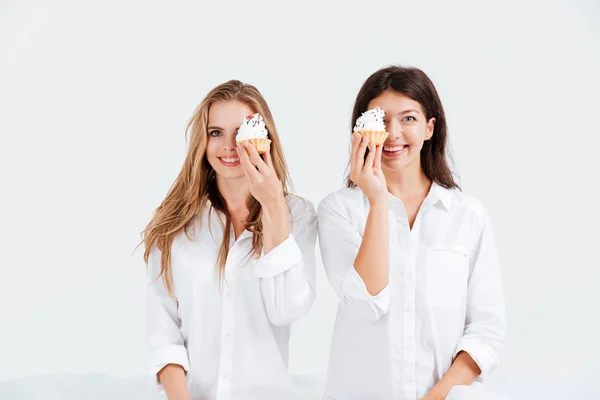 Due ragazze allegre che tengono dolci muffin mentre sono a letto — Foto Stock