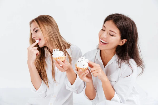 Dwie młode dziewczyny w białe koszule, gryzienie słodkie babeczki — Zdjęcie stockowe