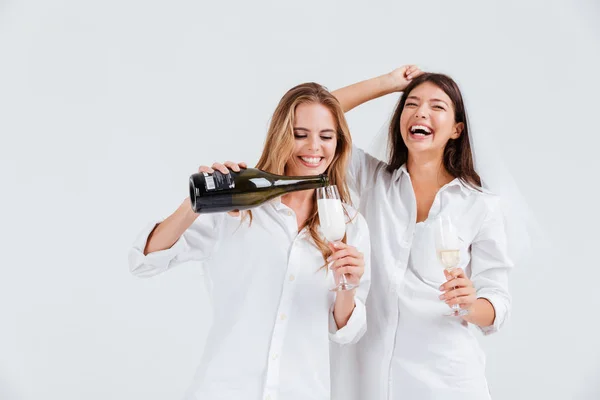 Two attractive women celebrating wedding with champagne bottle wearing veil — Stock Photo, Image