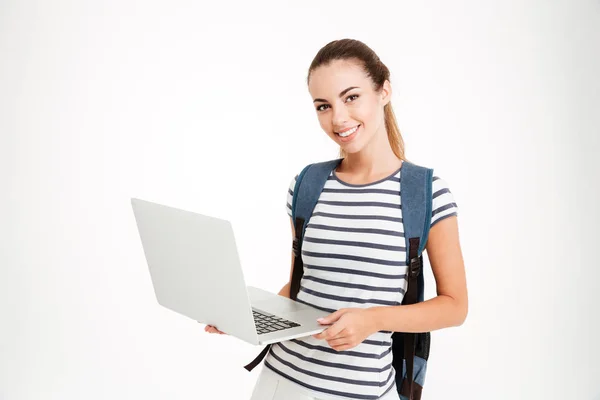 Feliz chica linda estudiante con mochila de pie y la celebración de la computadora portátil — Foto de Stock