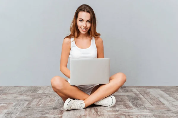Uśmiechnięta kobieta siedzi na podłodze z laptopa — Zdjęcie stockowe