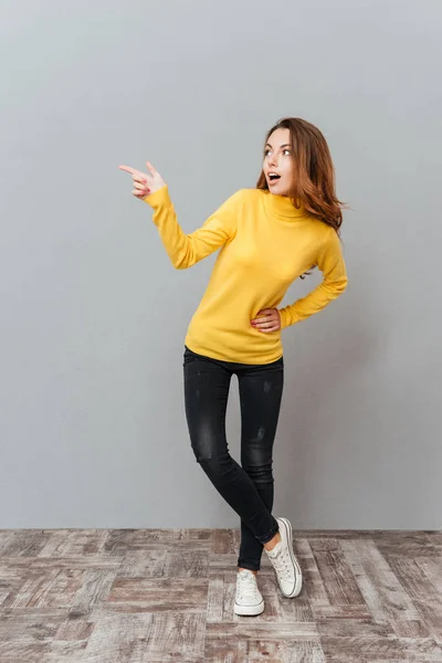 Jeune femme excitée en pull jaune debout et pointant du doigt — Photo