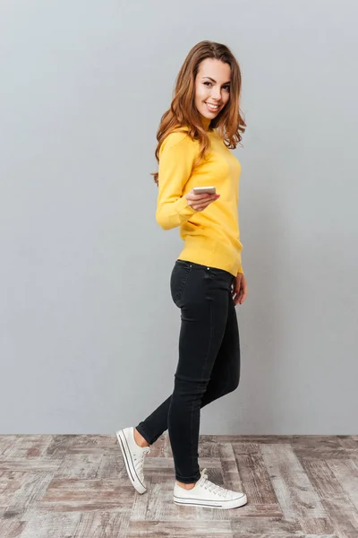 Happy usmívající se žena ve žlutém svetru s mobilním telefonem — Stock fotografie