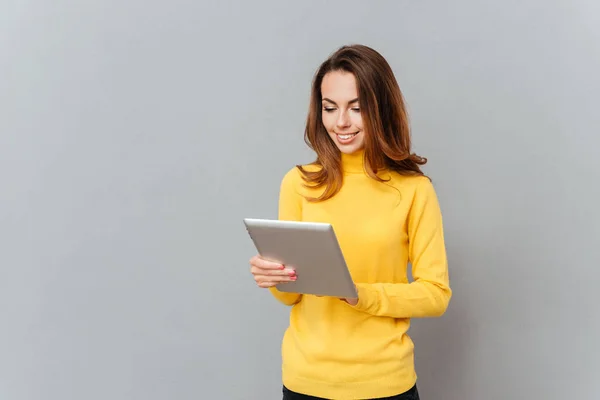 Sorrindo jovem mulher em suéter amarelo usando computador tablet — Fotografia de Stock