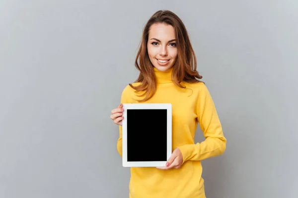 Женщина в жёлтом свитере показывает планшетный компьютер с чистым экраном — стоковое фото
