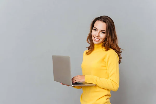 Mulher sorridente usando computador portátil e olhando para a câmera — Fotografia de Stock