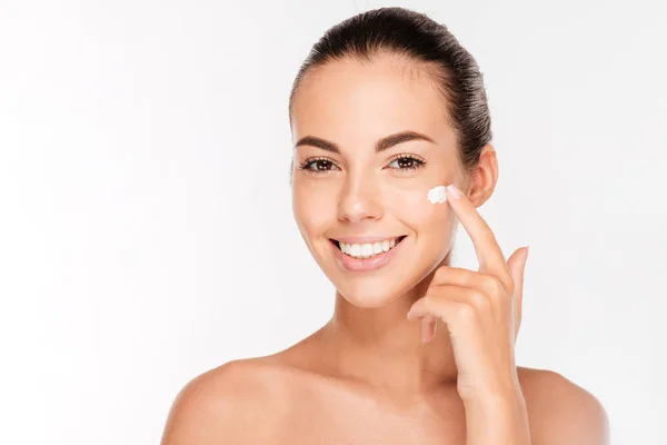 Beautiful young woman applying cosmetic cream treatment on her face — Stock Photo, Image