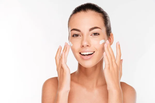 Beautiful young woman applying cosmetic cream treatment on her face — Stock Photo, Image