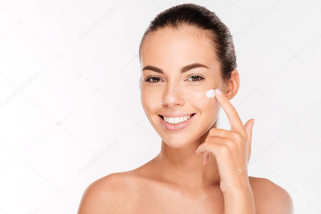 Beautiful young woman applying cosmetic cream treatment on her face