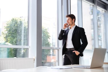 Ayakta ve Office cep telefonuyla konuşurken gülümseyen iş adamı