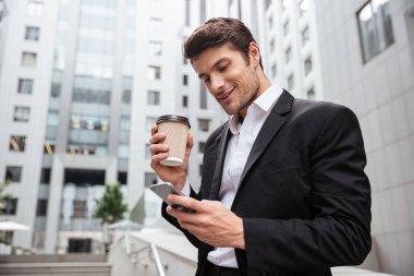 Genç işadamı içme kahve gülümseyen ve cep telefonu açık havada kullanma