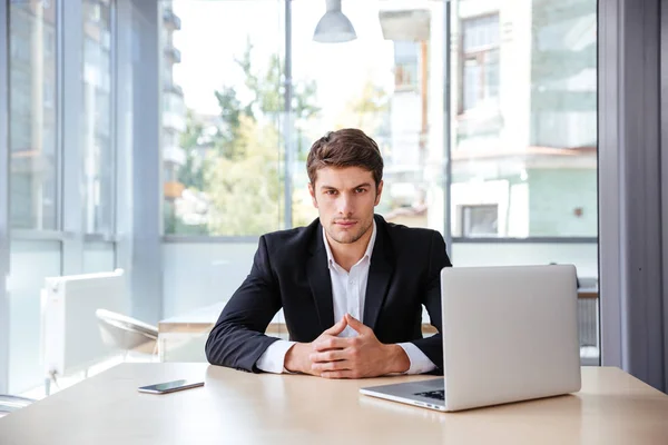 Poważny młody biznesmen z laptopa siedząc w biurze — Zdjęcie stockowe