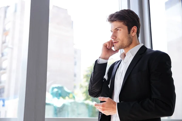 Uomo d'affari che parla sul cellulare vicino alla finestra in ufficio — Foto Stock