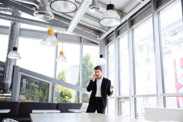 Cheerful young businessman talking on mobile phone and celebrating success — Stock Photo, Image