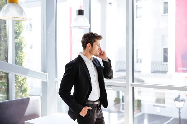 Empresario de pie cerca de la ventana y hablando por teléfono celular — Foto de Stock