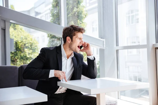 Mad angry young businessman sitting and shouting in cell phone — Stock Photo, Image