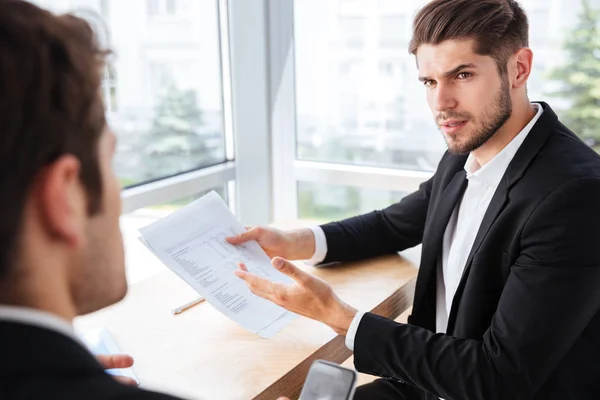 Businessman sitting and giving documents to his colleague in office — Stock Photo, Image