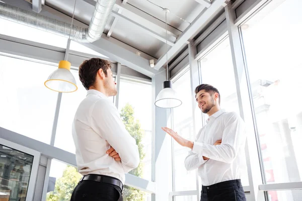 Два привлекательных молодых бизнесмена разговаривают в офисе — стоковое фото